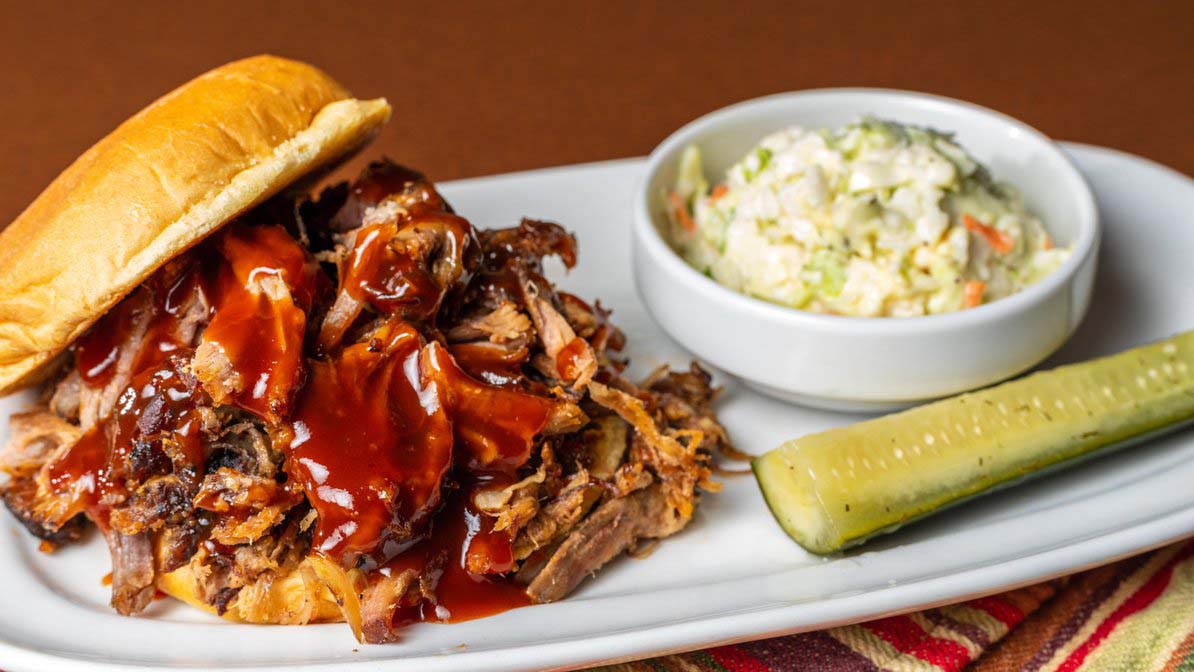 Hand=Held Pulled Pork Sandwich with potato salad and pickle
